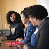 Three colleagues laughing together around a table with laptops