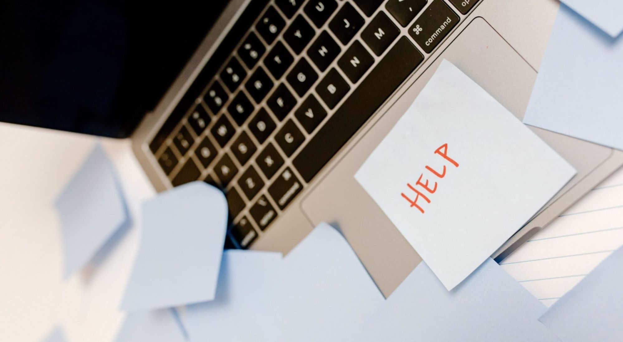 A sticky note that says help on a laptop keyboard