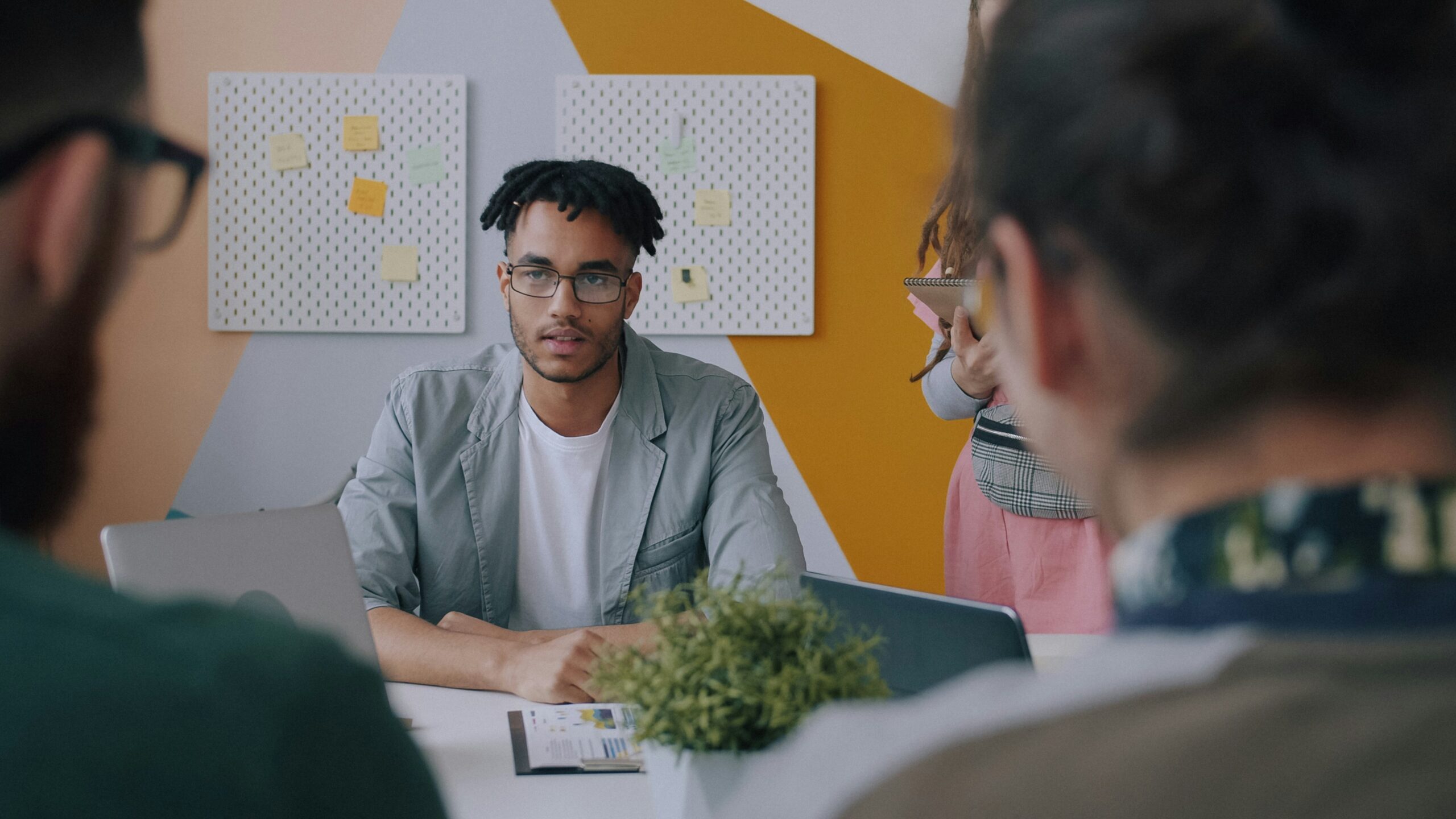 A colleague writing on a flipchart while two people watch from a meeting table