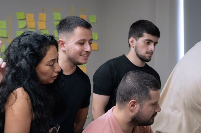 Four colleagues looking at a screen together in front of a wall of sticky notes