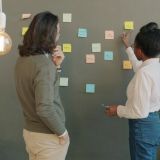 Two people arranging sticky notes on a wall