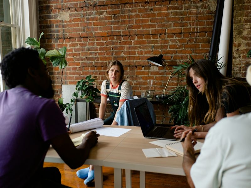Five colleagues in discussion around a table in a brick walled meeting room
