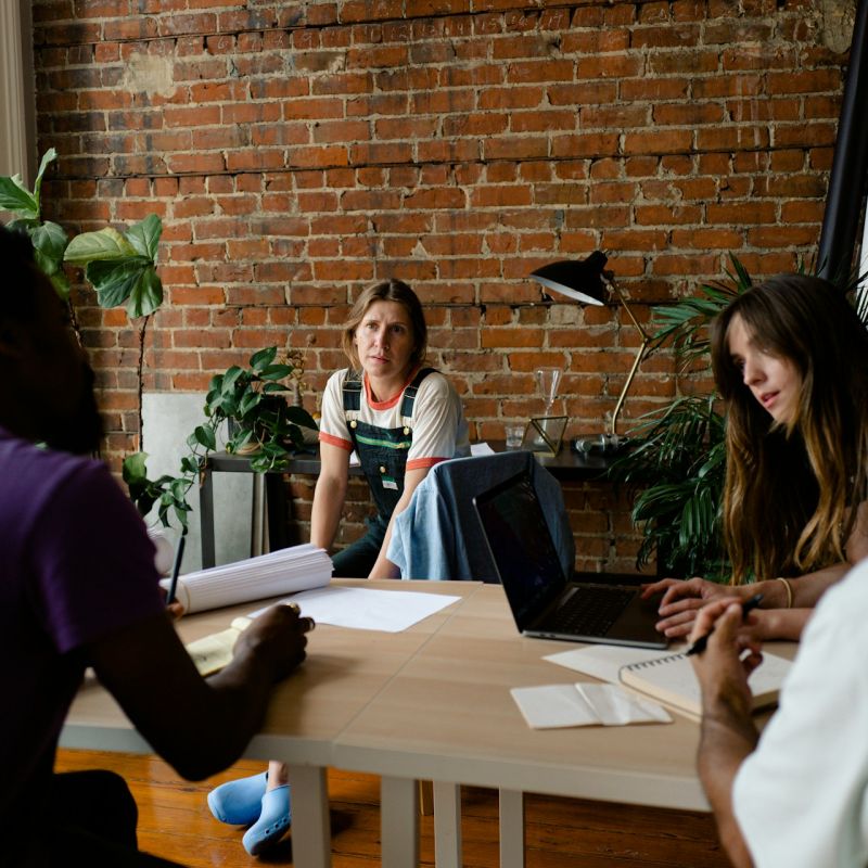 Five colleagues in discussion around a table in a brick walled meeting room